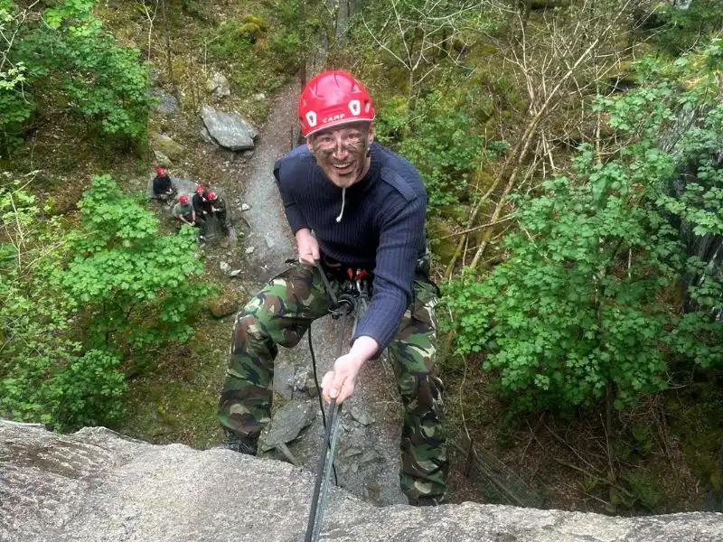A man looking up at the camera and smiling as he abseils down a steep ledge