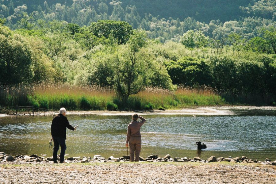 Couple standing by Derwentwater watching their dog in the water