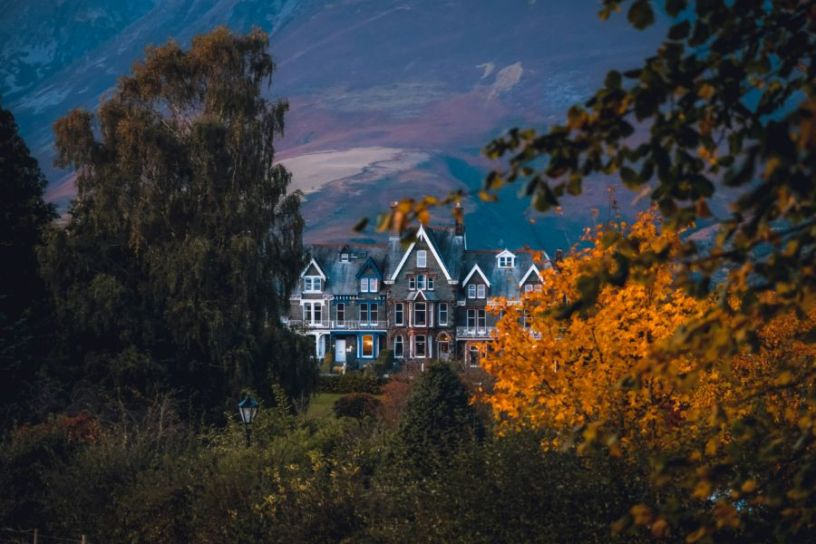 Slate-clad buildings in Keswick seen through some Autumn trees, with the slopes of Skiddaw in the background.